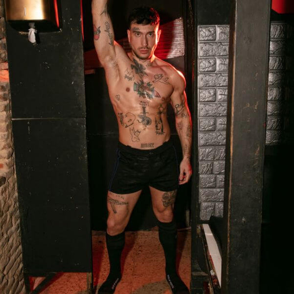 Man with tattoos standing in a doorway with a brick wall background
