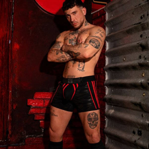 Man with tattoos wearing black and red shorts against a dark background