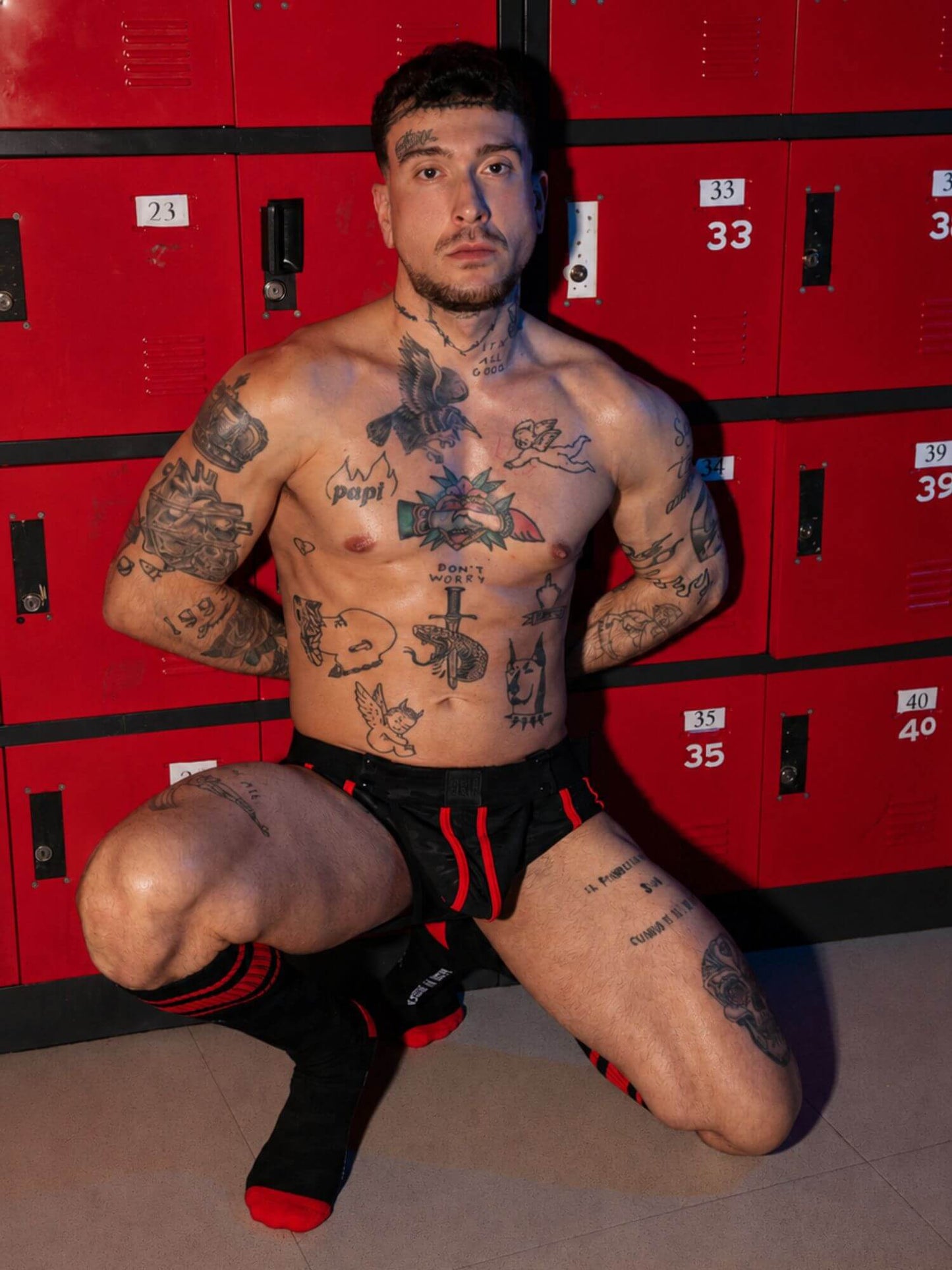 Man with tattoos posing in front of red lockers