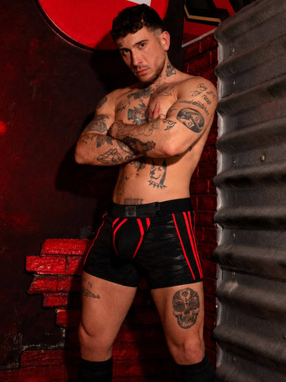 Man with tattoos wearing black and red underwear against a dark background