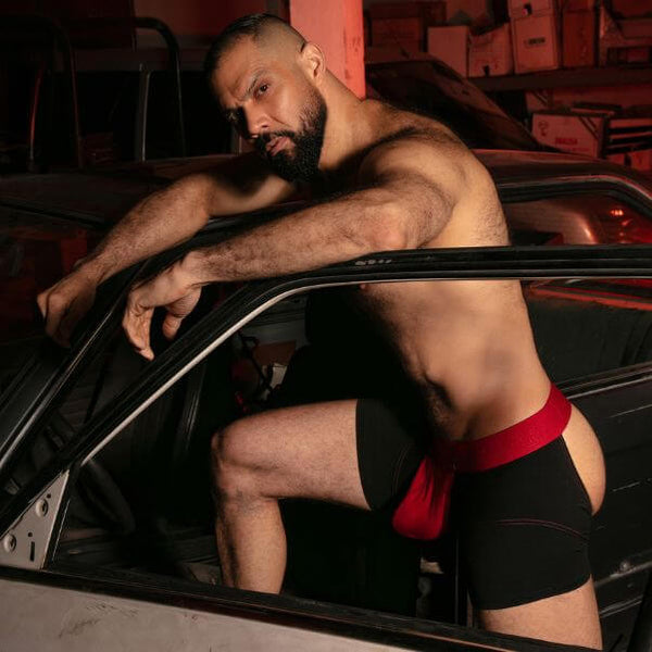 Man in black and red underwear sitting inside a car with open door.