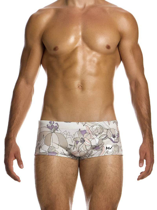A model wearing a pair of swim trunks with a floral outline sketch in art nouveau design, predominantly in pastel mint or lilac shades.