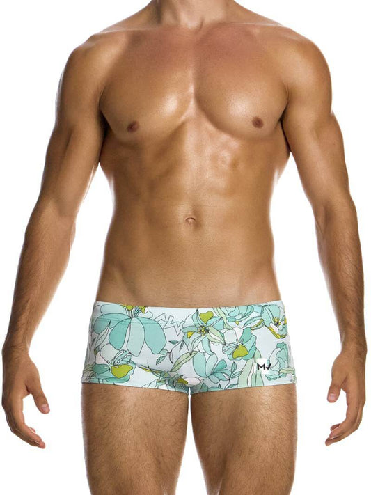 A model wearing a pair of swim trunks with a floral outline sketch in art nouveau design, predominantly in pastel mint or lilac shades.