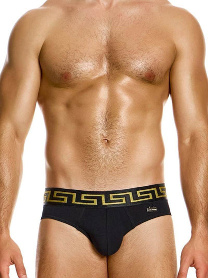 A model wearing black Modus Vivendi Meander briefs with a gold and silver Greek key print on the waistband and a brand charm logo.