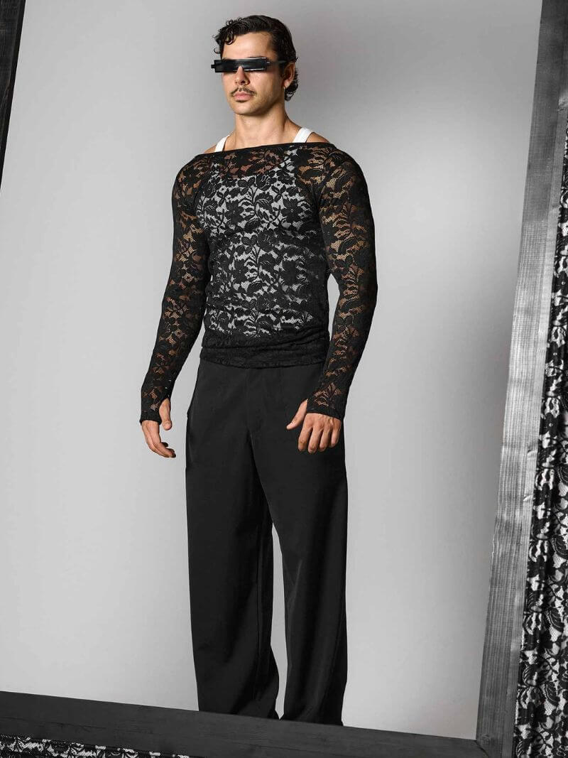 Person wearing a black lace long-sleeve top and black pants against a gray background