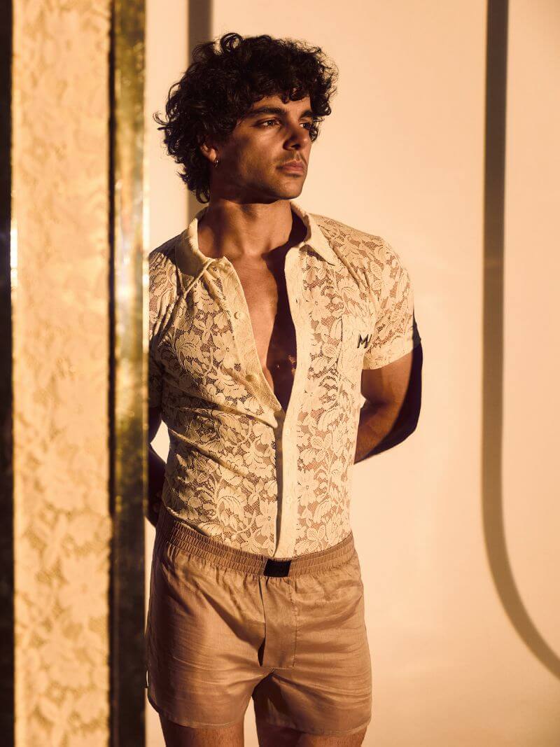Man wearing a patterned vest over a shirt with beige pants against a neutral background