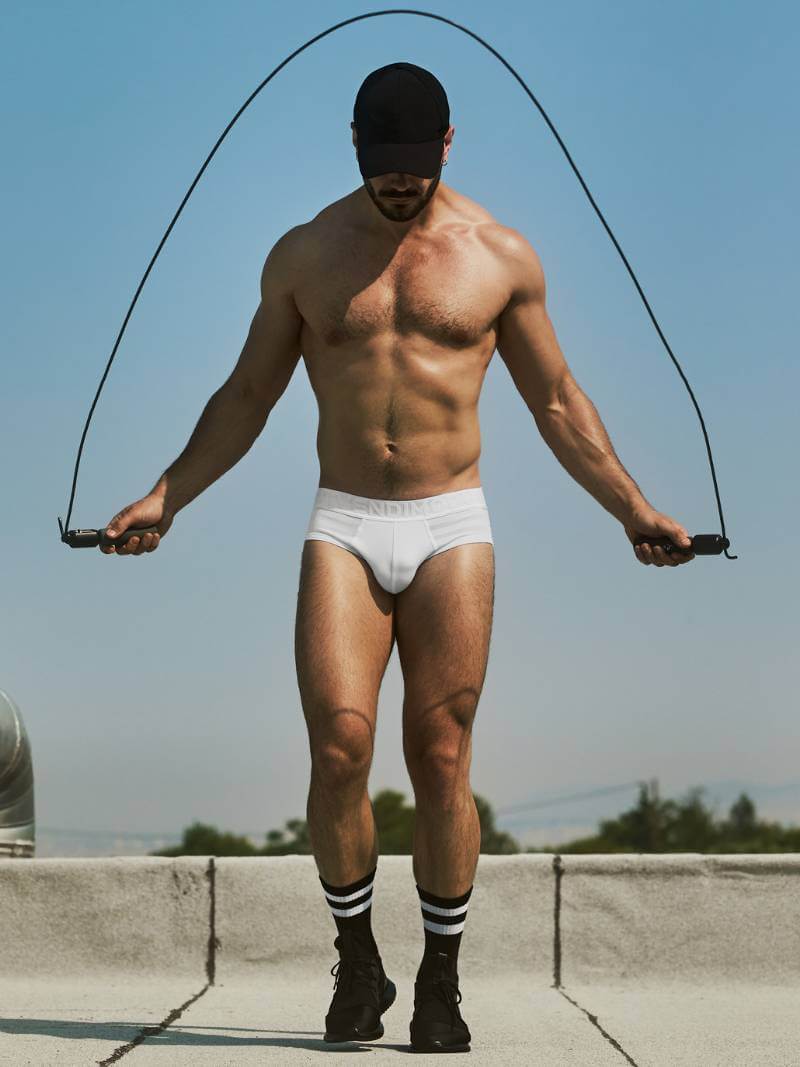 Man in white underwear and socks holding a jump rope against a clear blue sky.