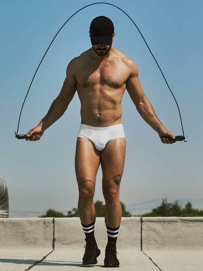 Man in white underwear and socks holding a jump rope against a clear blue sky.