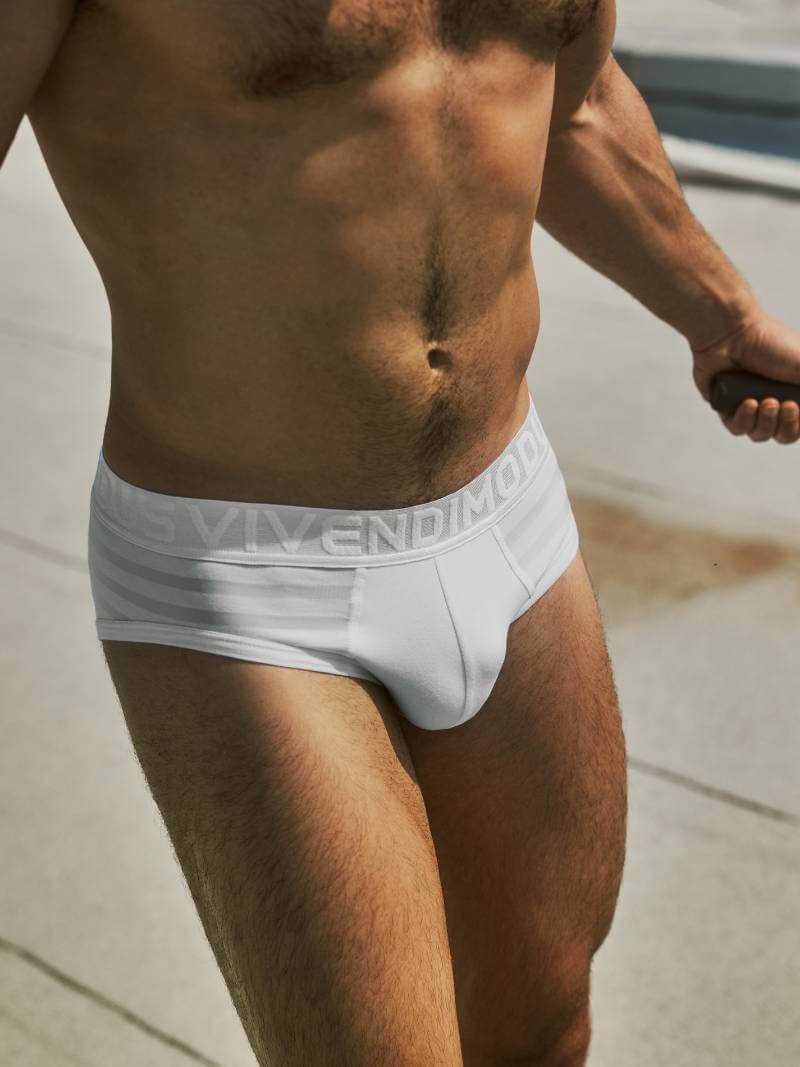 Man wearing white underwear with a brand logo, standing outdoors.