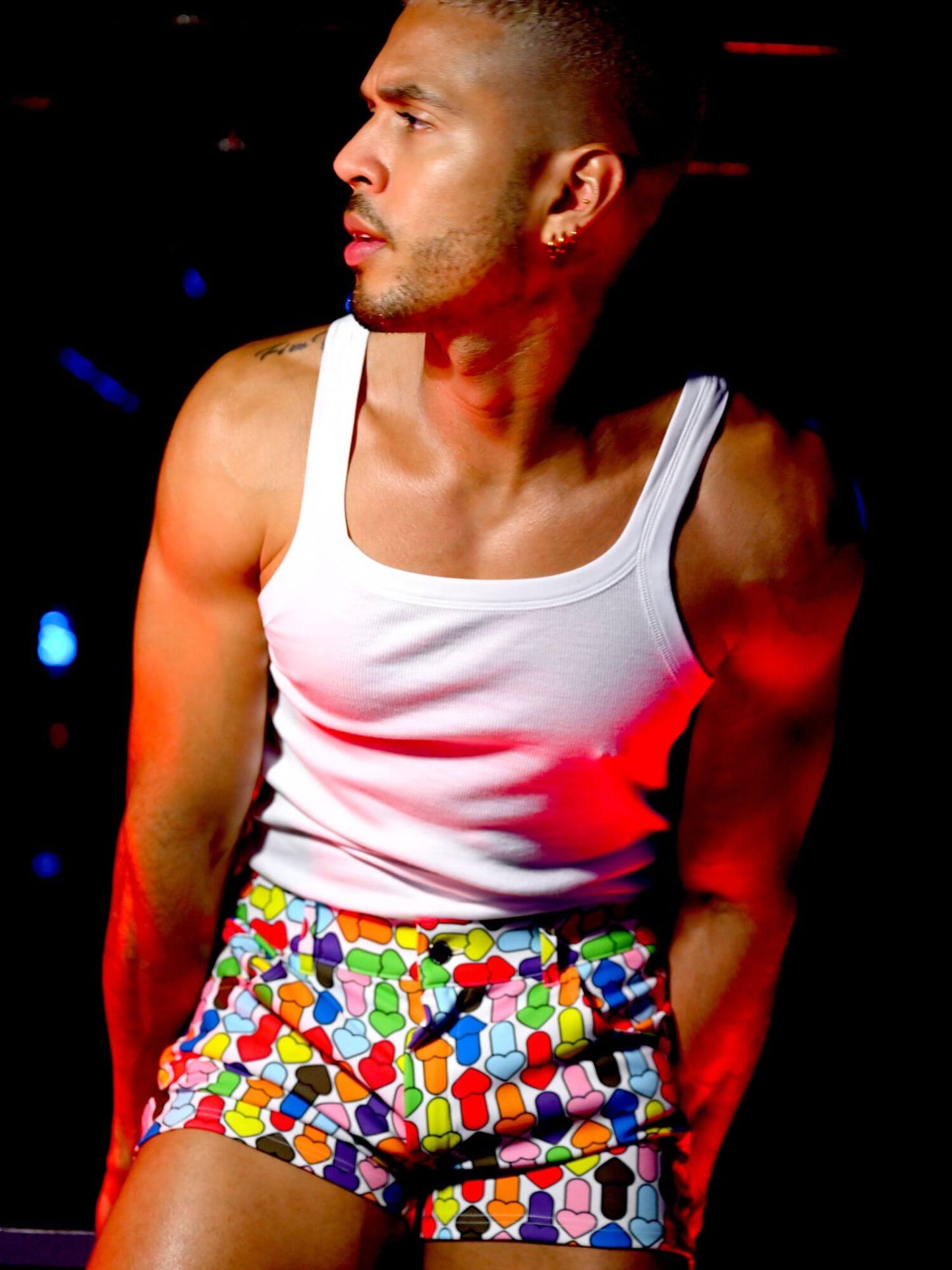 Person wearing a white tank top and colorful patterned shorts with a dark background