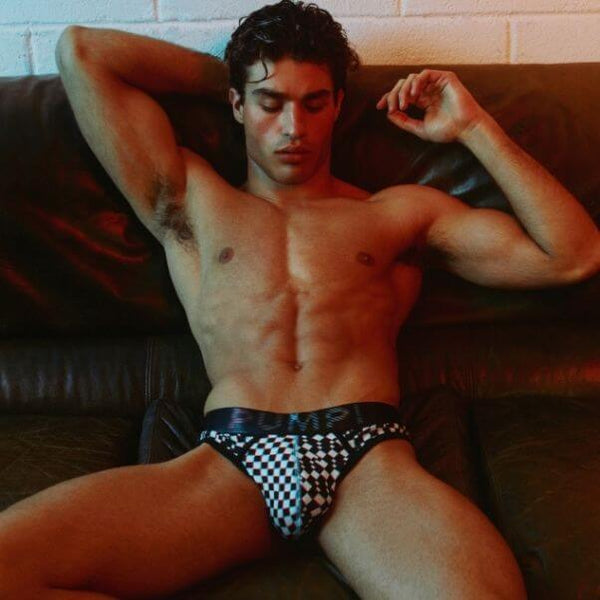 Man wearing checkered PUMP! Glitch underwear sitting on a couch with a blurred background