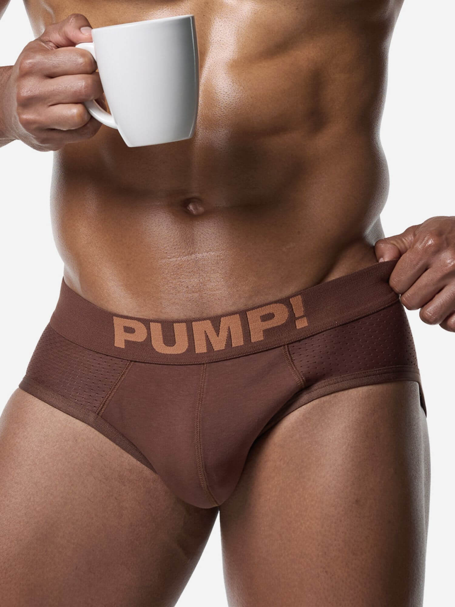 Person wearing brown underwear with 'PUMP!' text, holding a white mug.