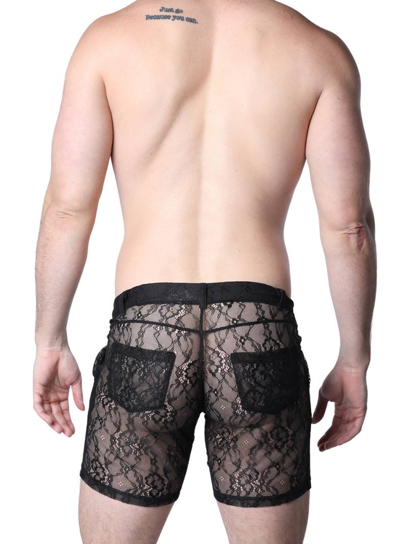 Man wearing black lace underwear standing against a textured wall.