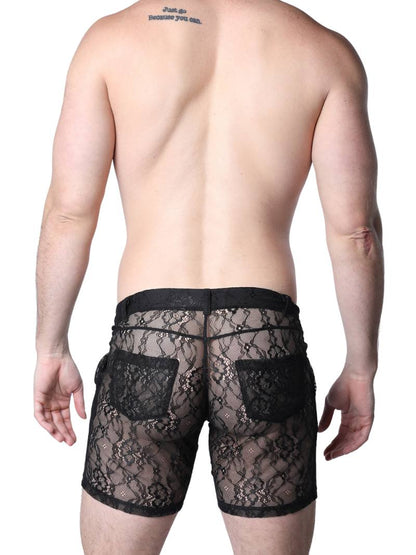Man wearing black lace underwear standing against a textured wall.