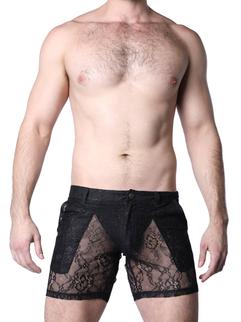 Man wearing black lace underwear standing against a textured wall.