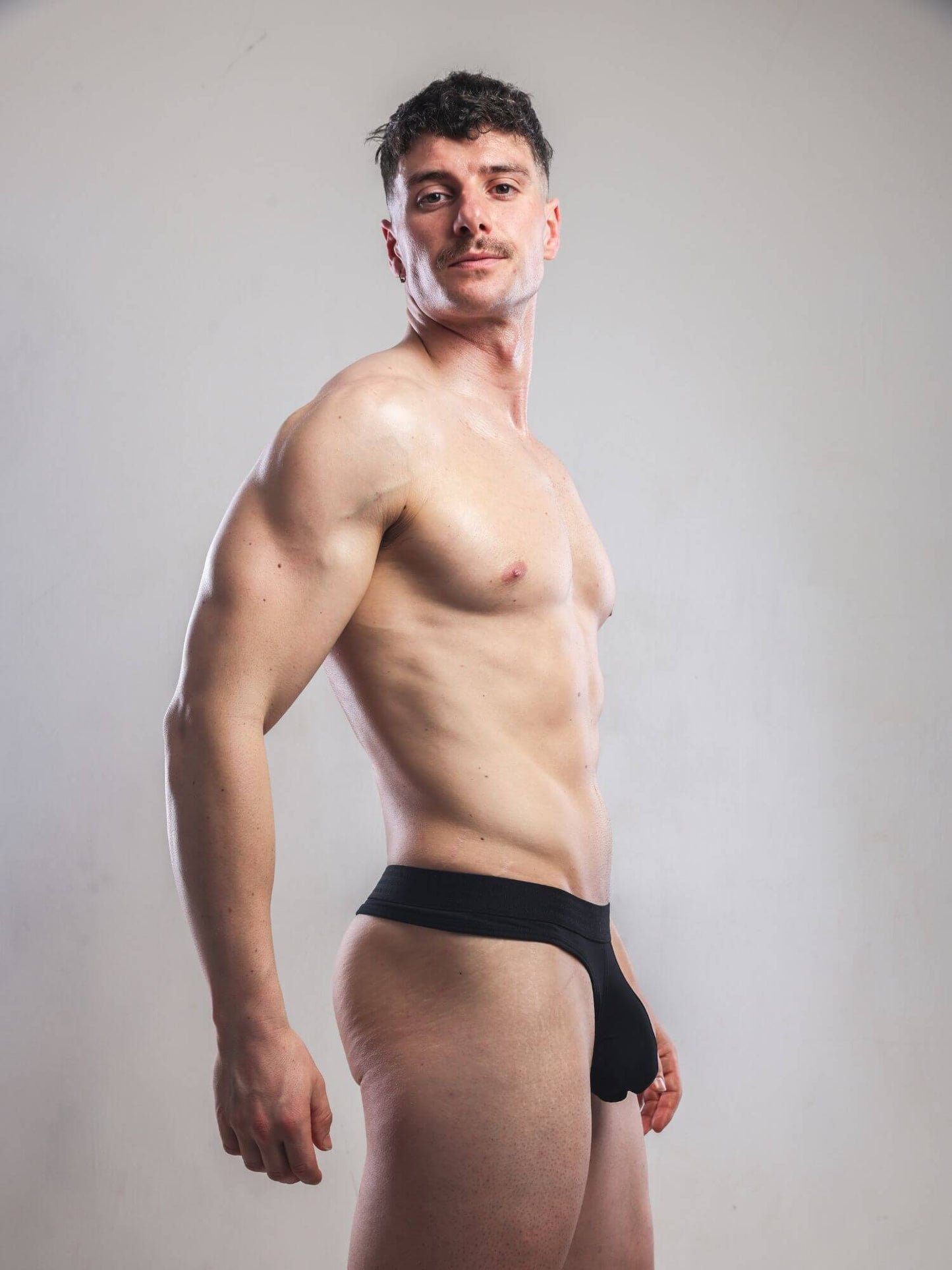Man wearing a black thong against a plain background