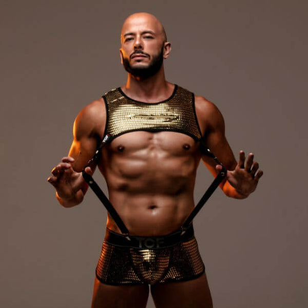 Man wearing a gold and black outfit with harnesses against a brown background