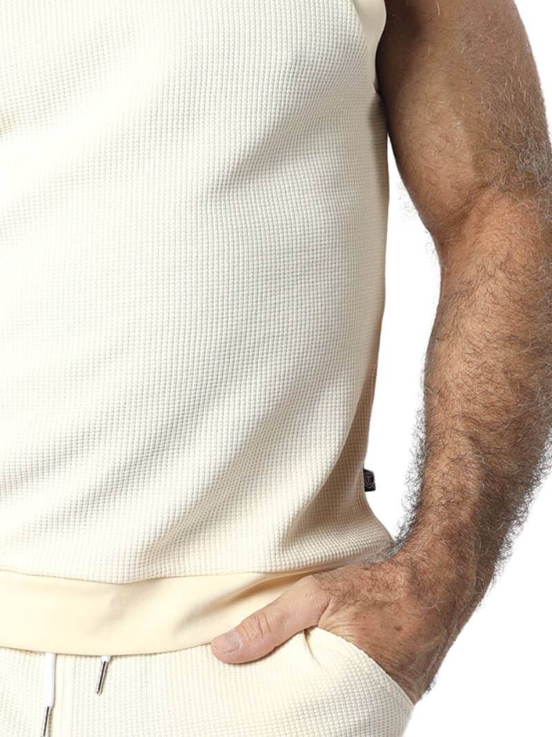 Person wearing a light-colored sleeveless shirt and pants on a white background
