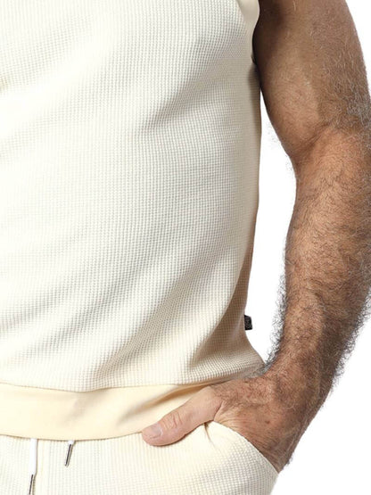 Person wearing a light-colored sleeveless shirt and pants on a white background