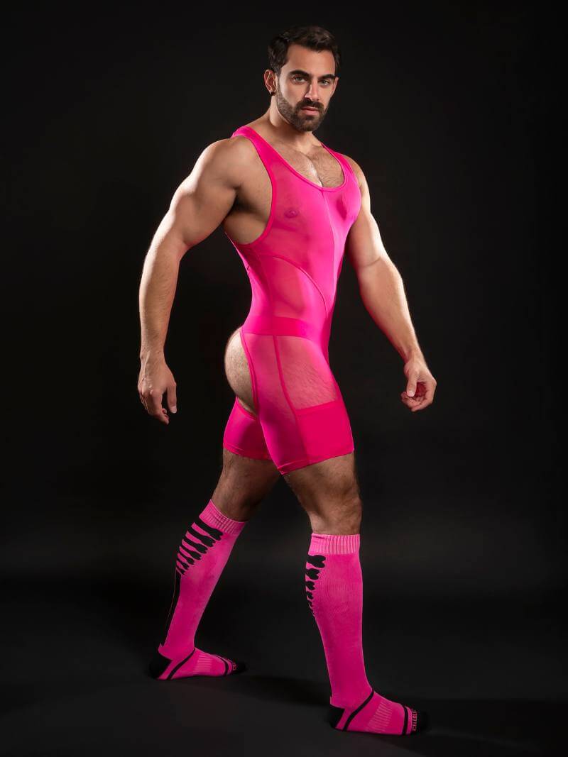 Man wearing a bright pink wrestling singlet and socks on a black background